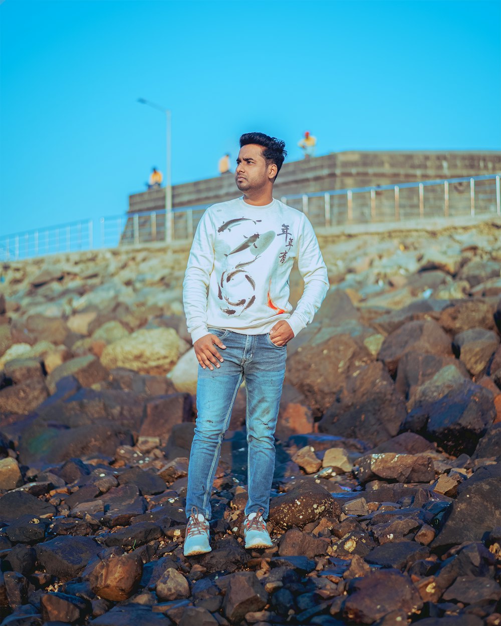 a man standing on a rocky beach with his hands in his pockets