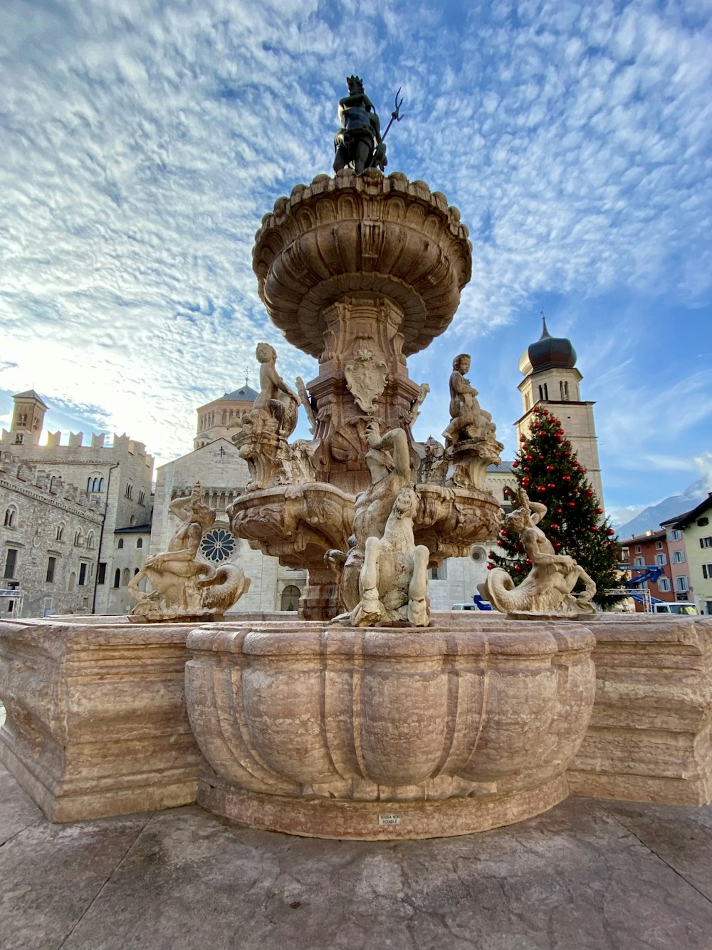 a fountain with statues and a christmas tree in the background