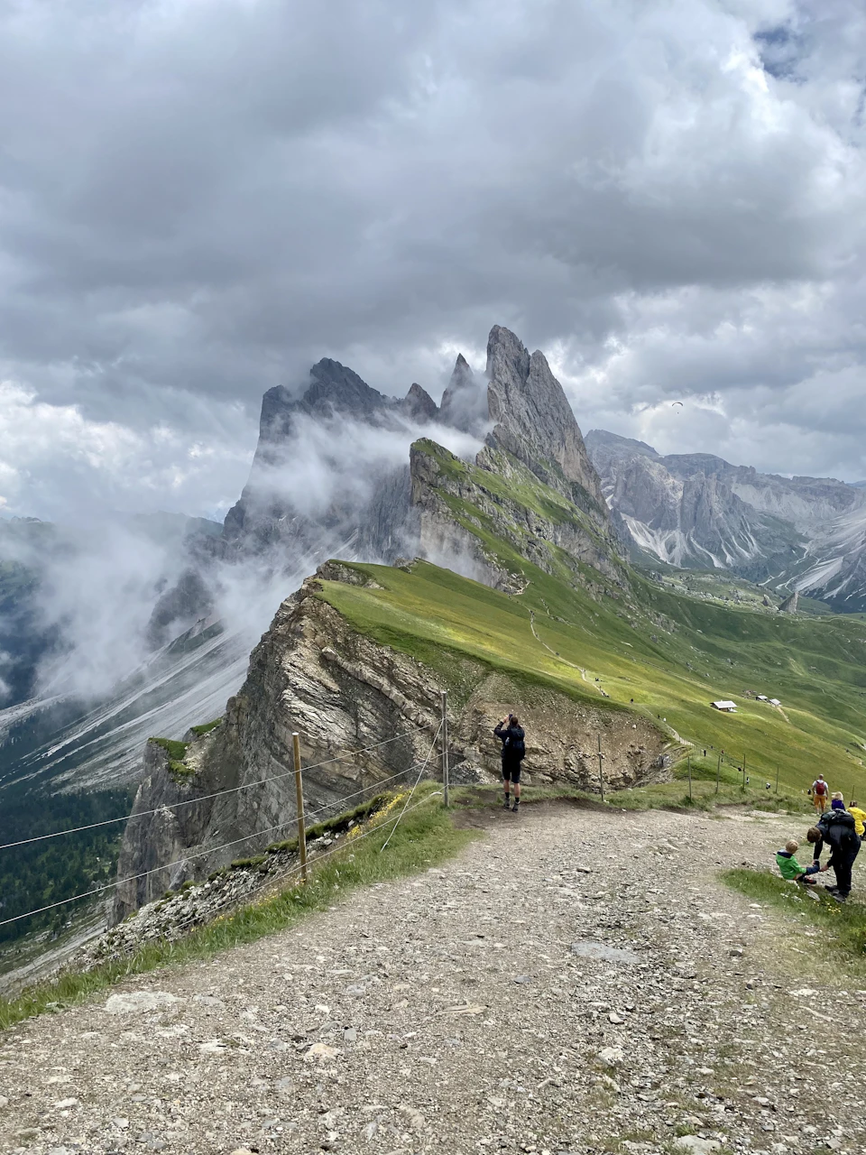 Group of people hiking up mountain trail surrounded by lush green vegetation and towering peaks