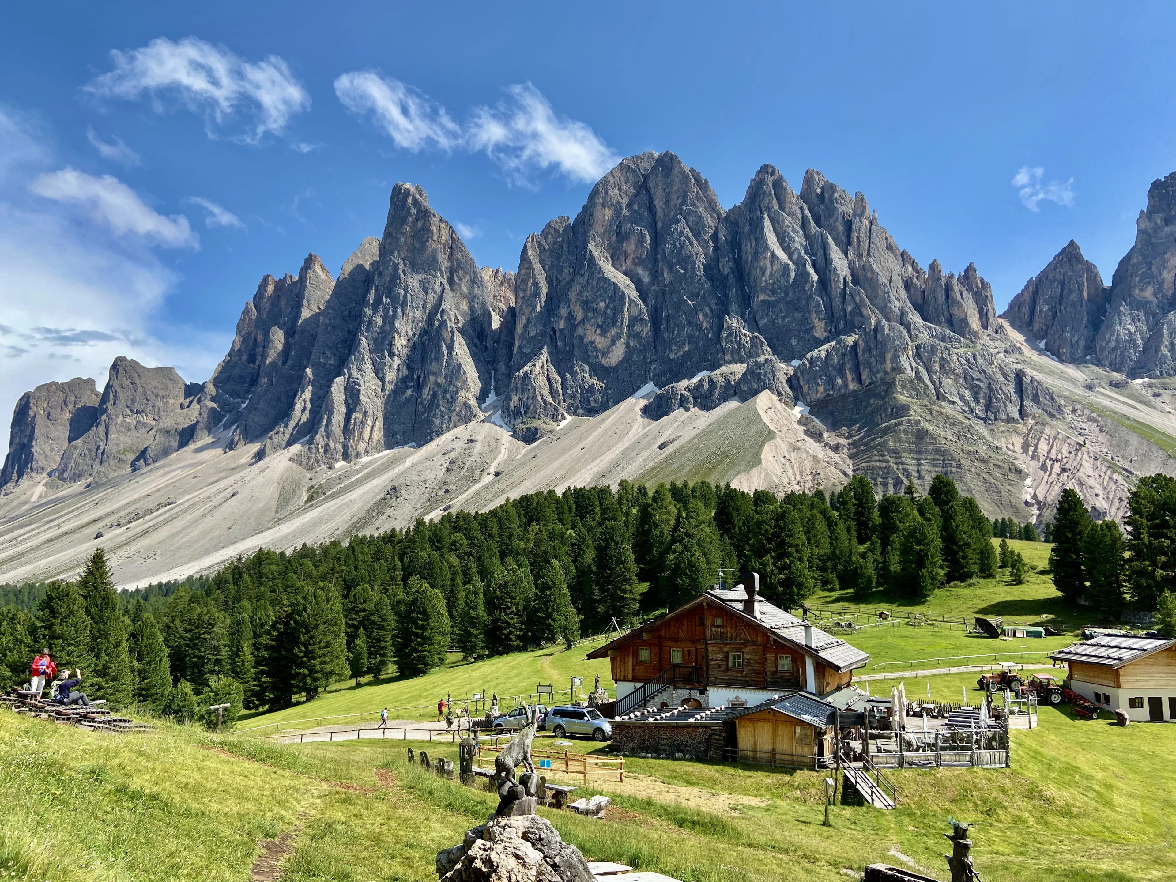 A wooden mountain hut in a green meadow beneath the jagged Odle peaks, Dolomites, Italy