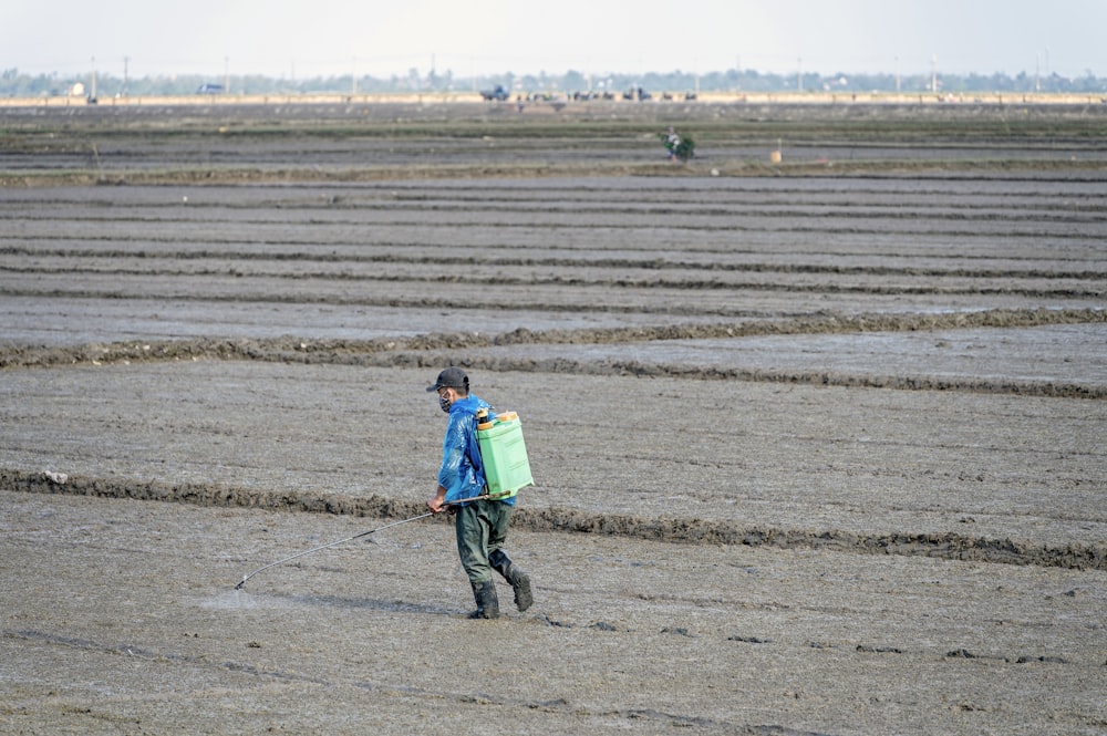 a man walking across a field carrying a green bag