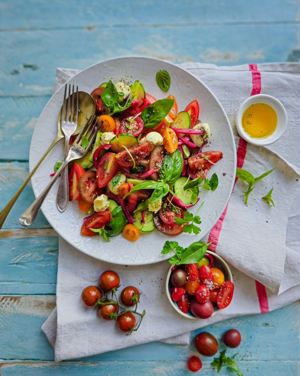 a white plate topped with a salad next to a bowl of tomatoes