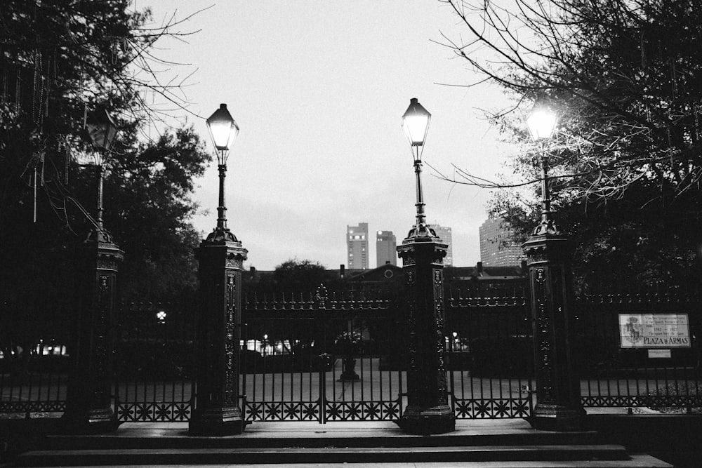 a black and white photo of a gate and street lights