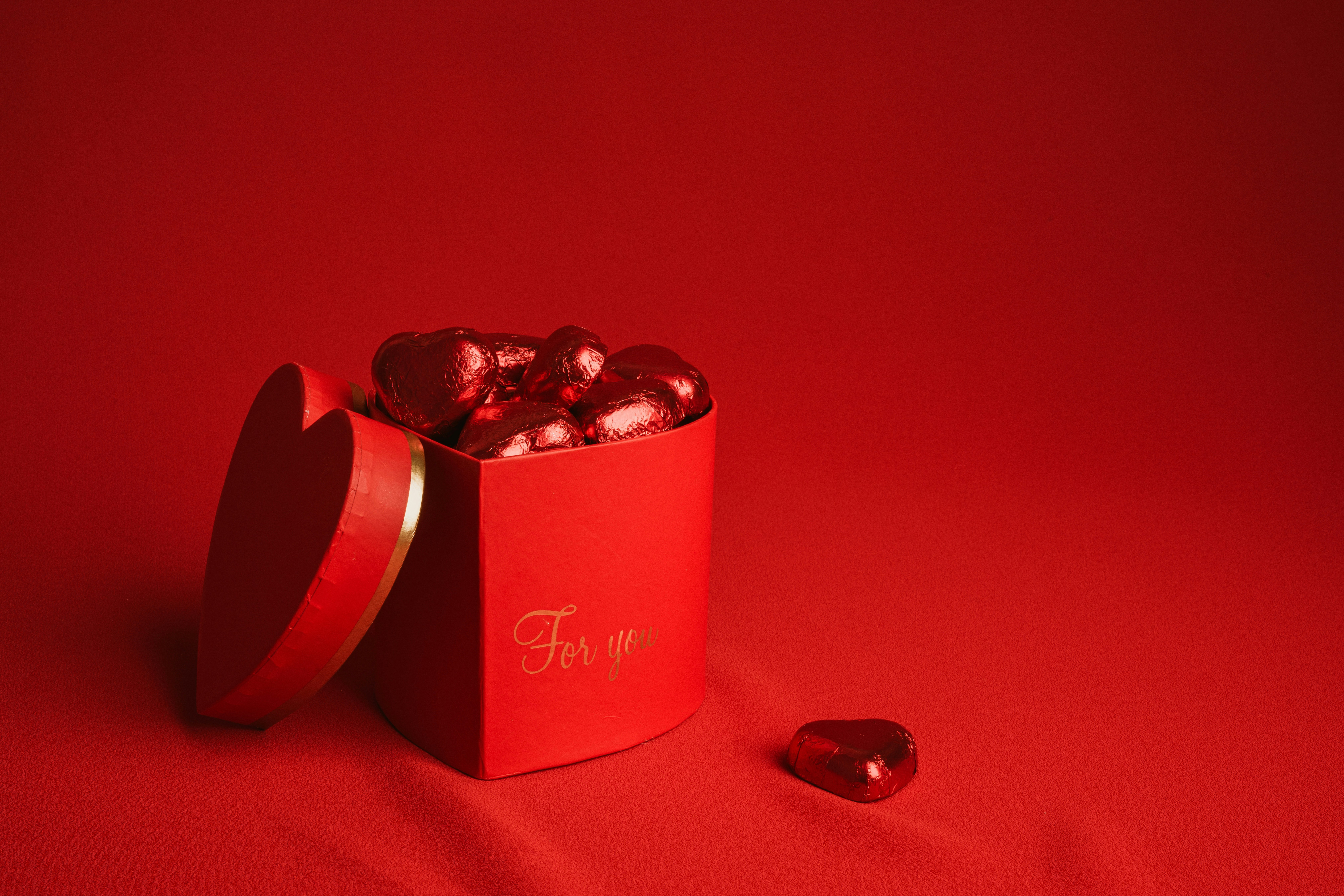 una scatola rossa piena di cuori di cioccolato su una superficie rossa
