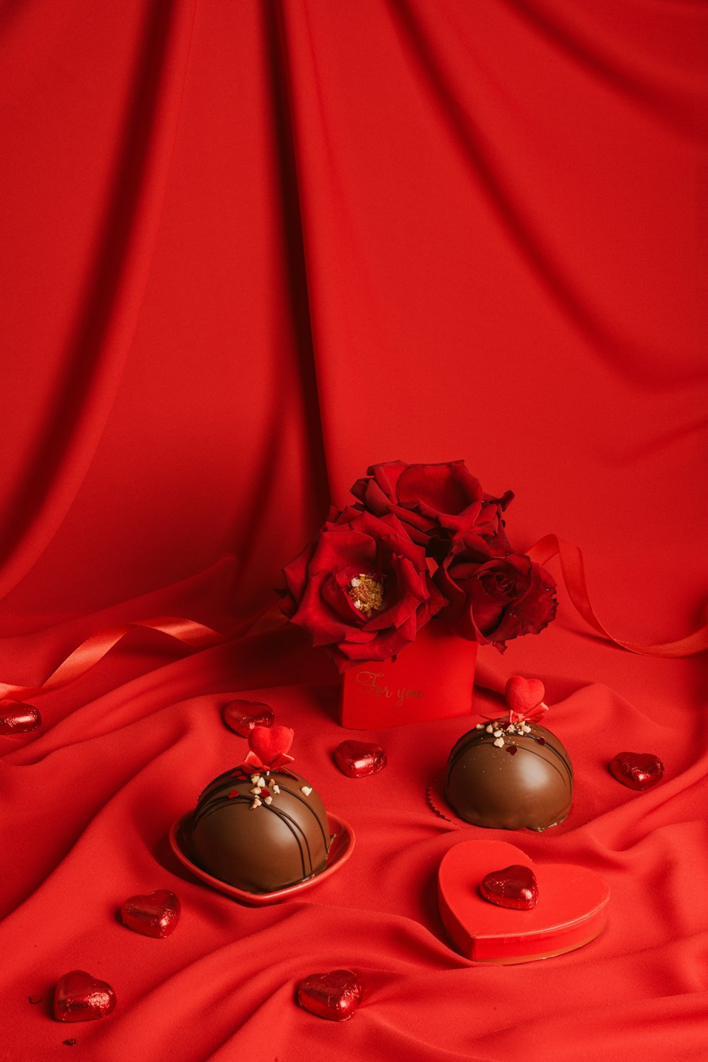 a vase of flowers and two chocolates on a red cloth
