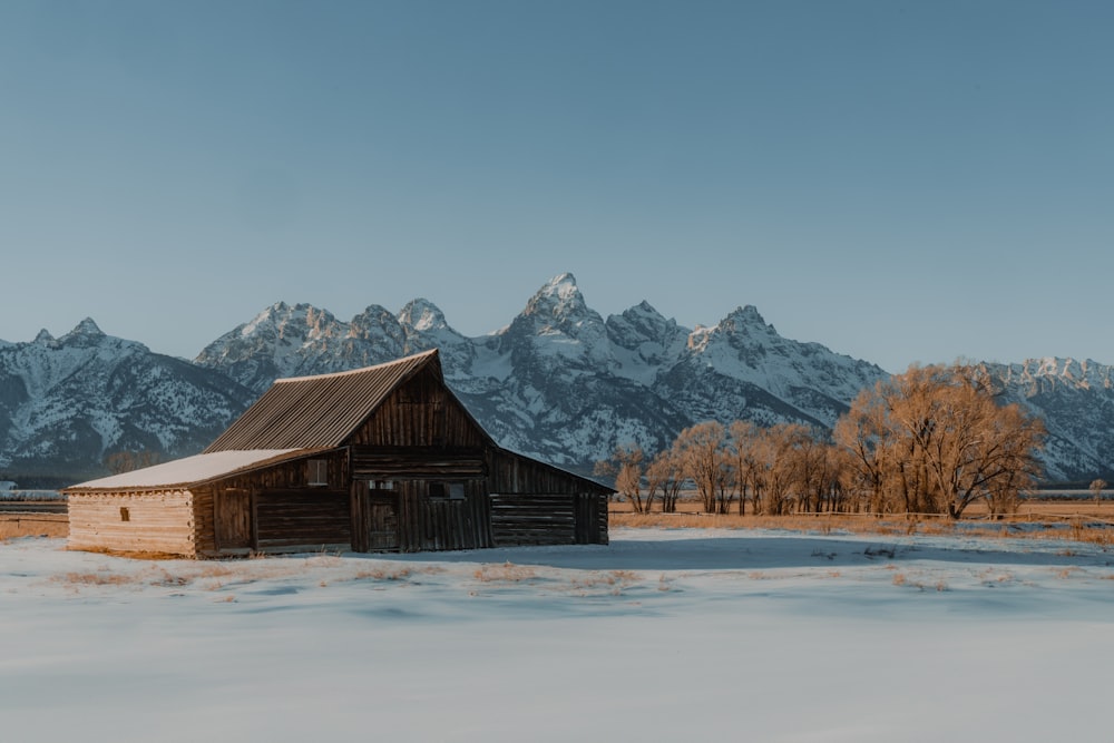 a barn in a snowy field with mountains in the background