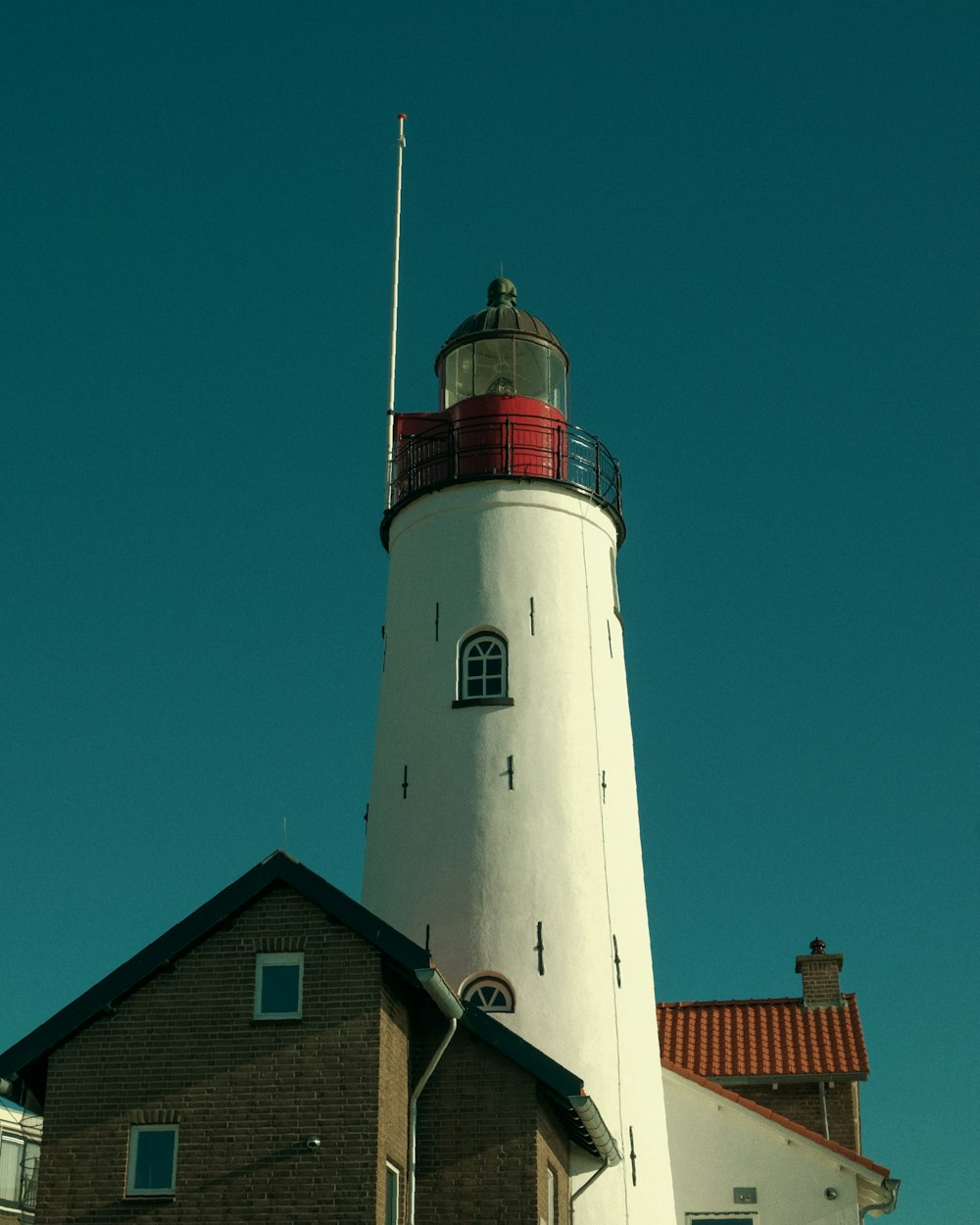 Ein weißer Leuchtturm mit roter Spitze vor blauem Himmel