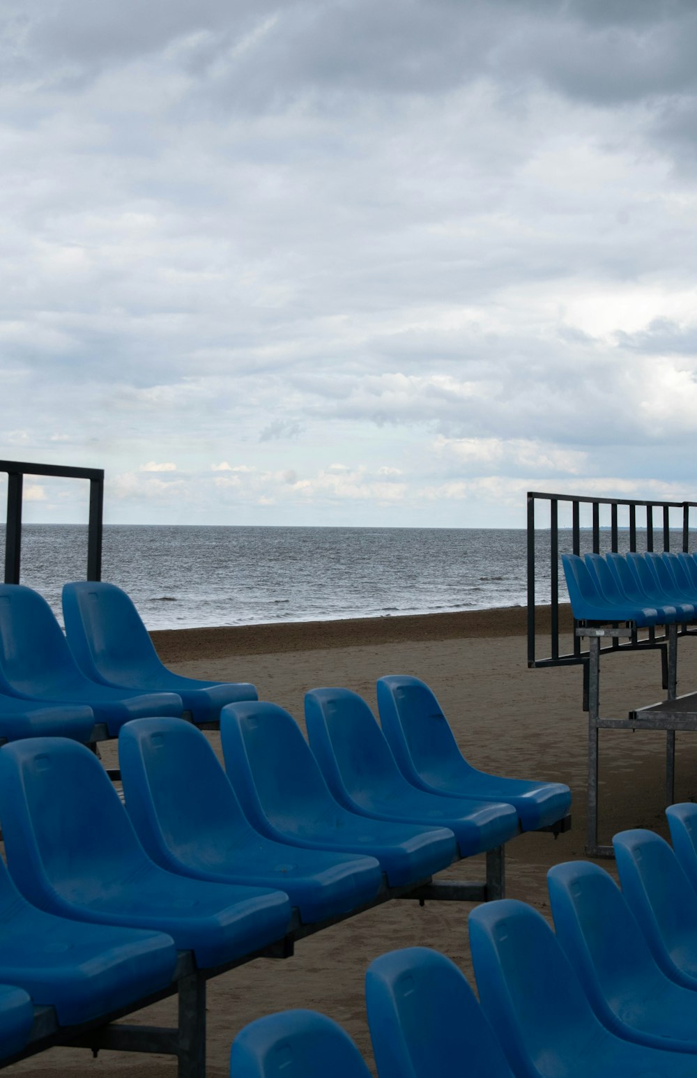 a row of blue chairs sitting on top of a sandy beach
