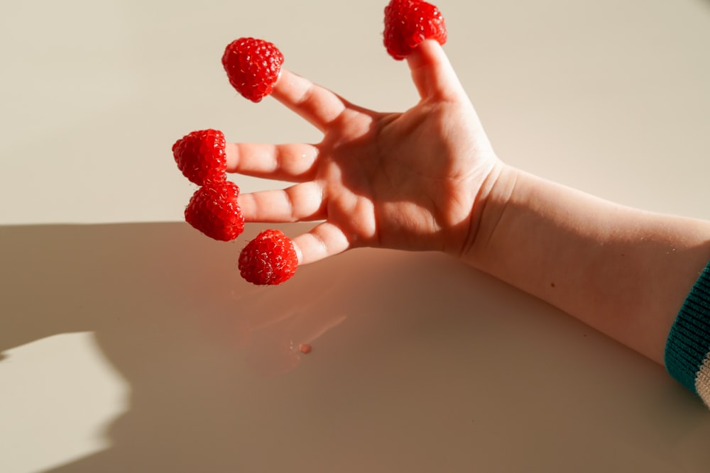 a person's hand holding raspberries on a table