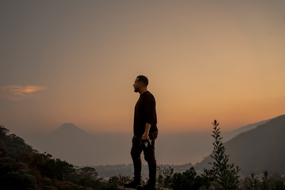 un homme debout au sommet d’une montagne au coucher du soleil