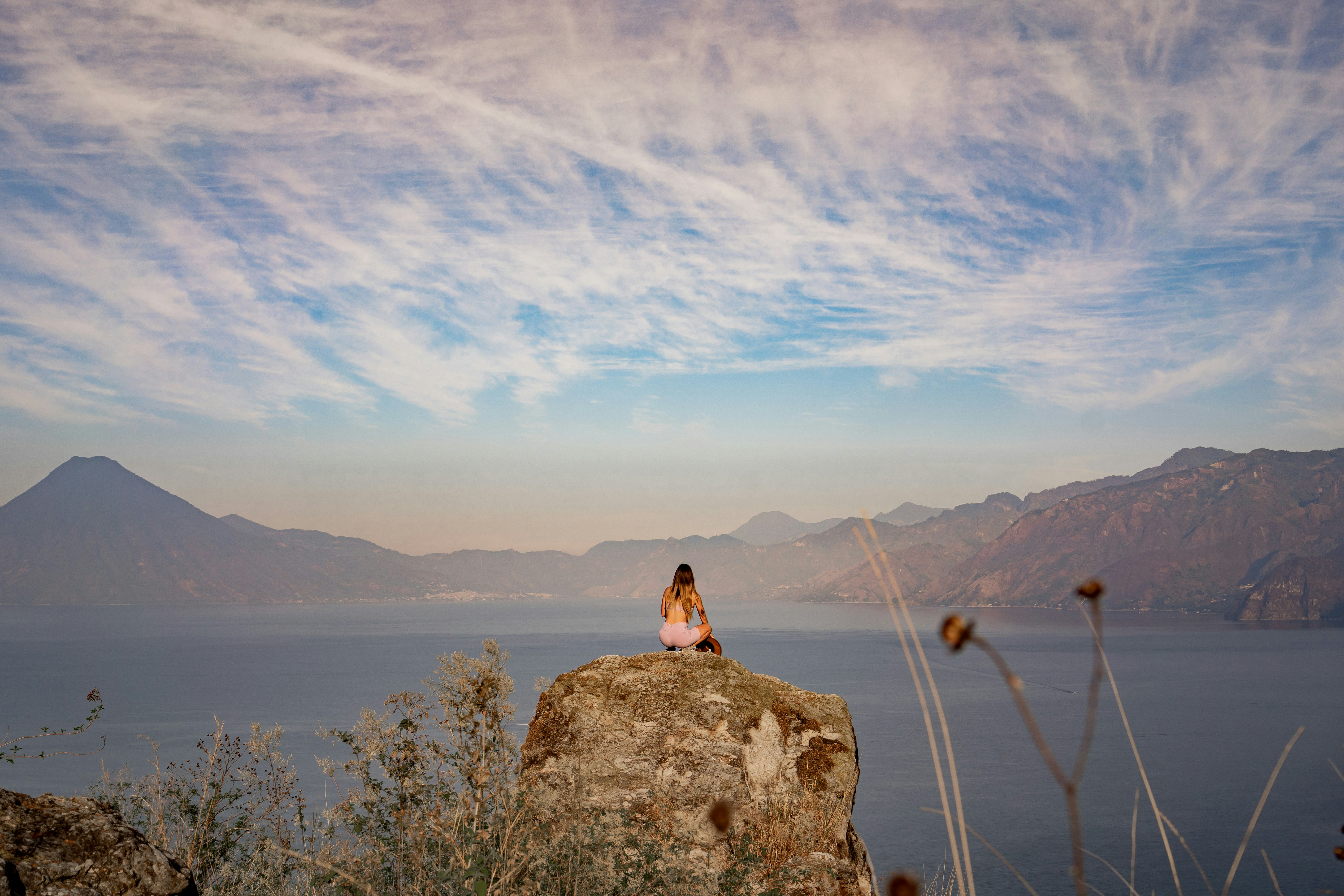 a woman sitting on top of a rock next to a body of water, 