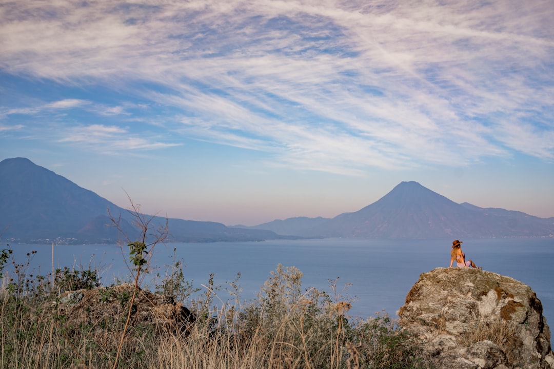 a woman sitting on top of a rock next to a body of water,