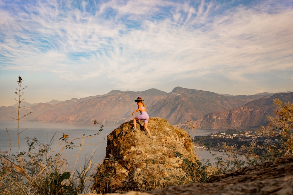 a woman sitting on top of a rock next to a body of water