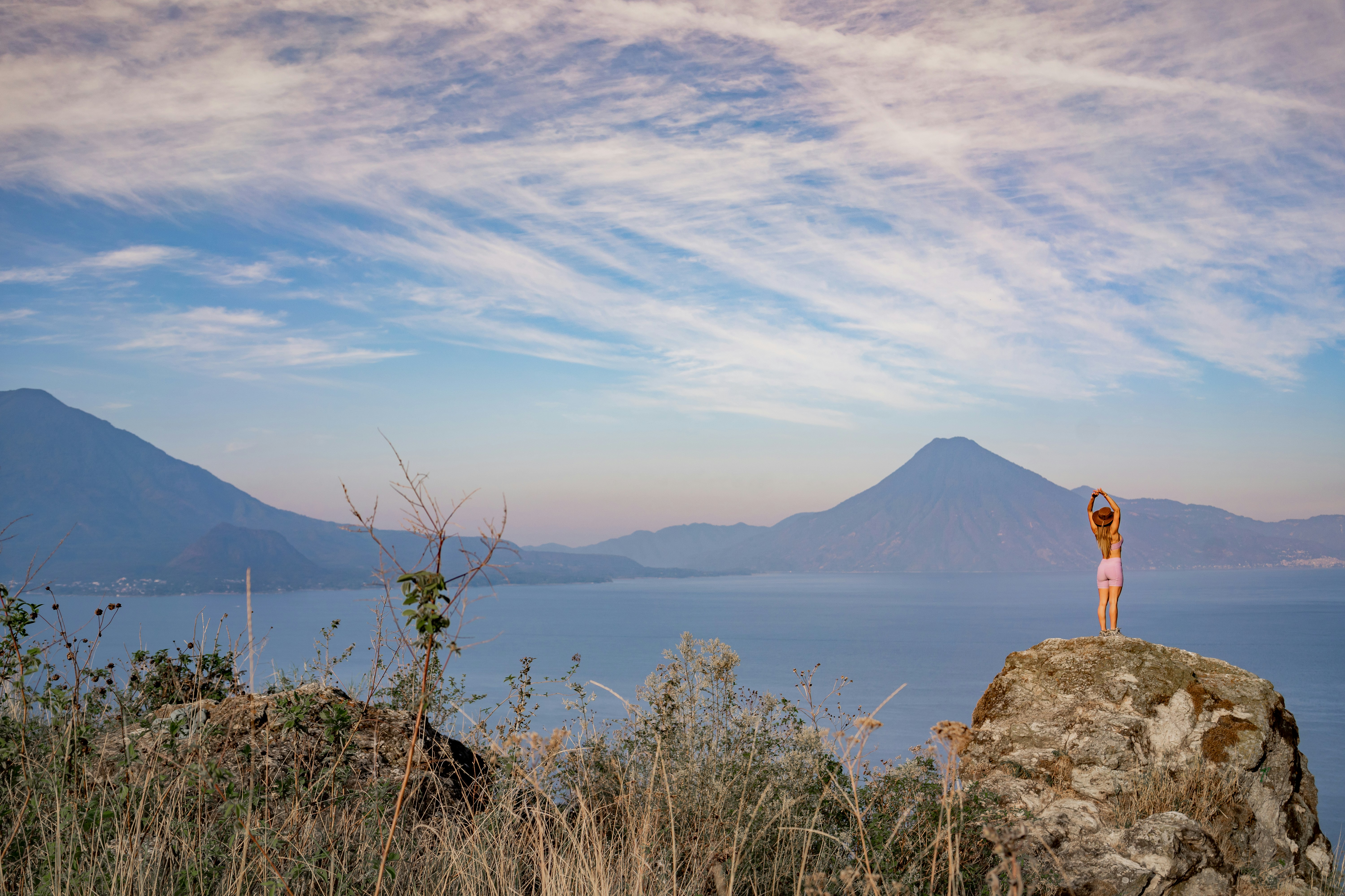 Una mujer de pie en lo alto de una roca junto a un cuerpo de agua