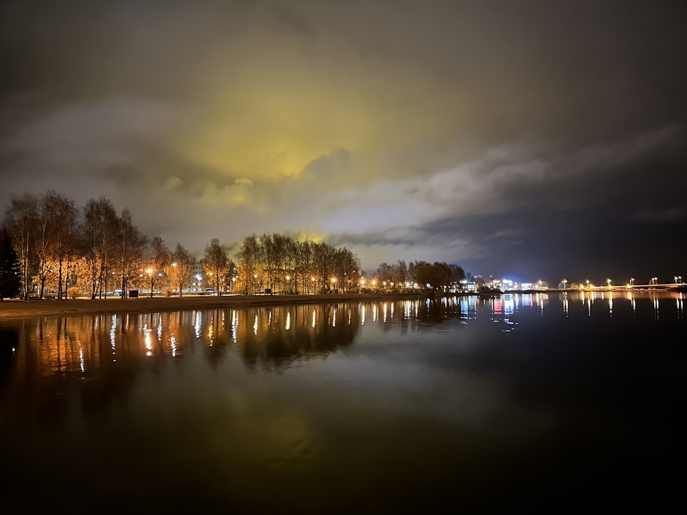 a body of water with trees and lights in the background