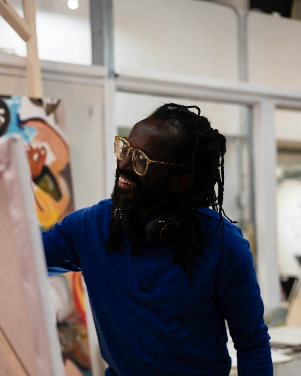a man with dreadlocks smiles while standing in front of a easel