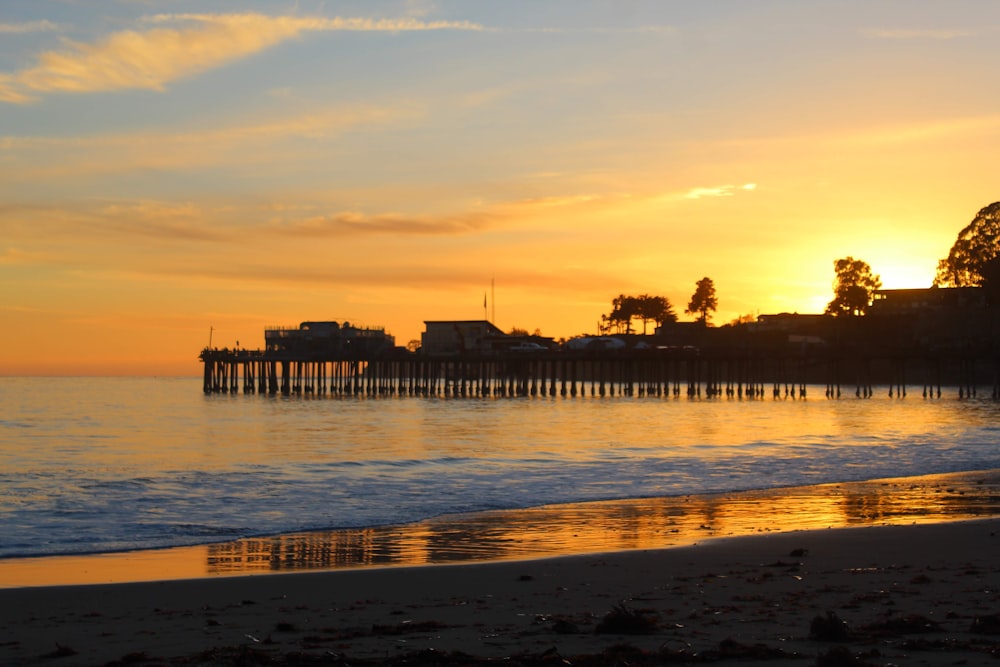 the sun is setting over the ocean with a pier in the distance