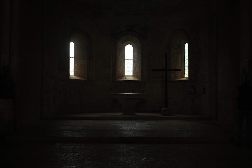 a dark room with three windows and a cross