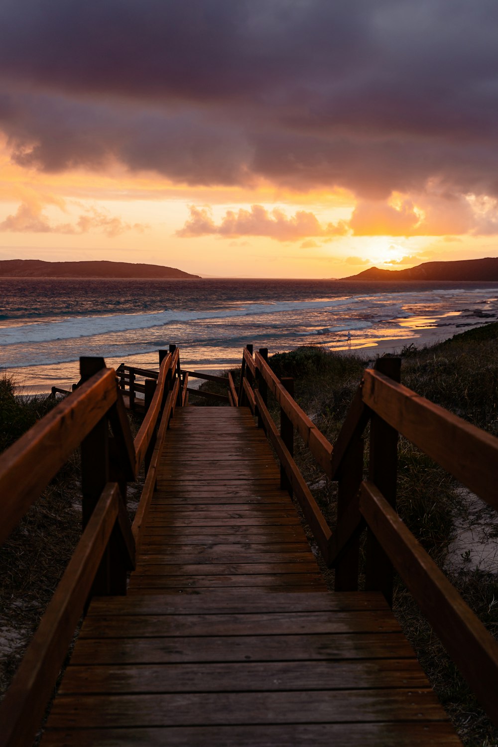 a wooden walkway leading to the beach at sunset