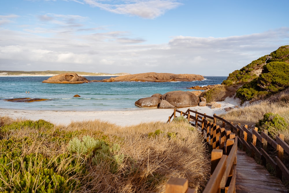 a wooden walkway leading to a beach with large rocks in the background