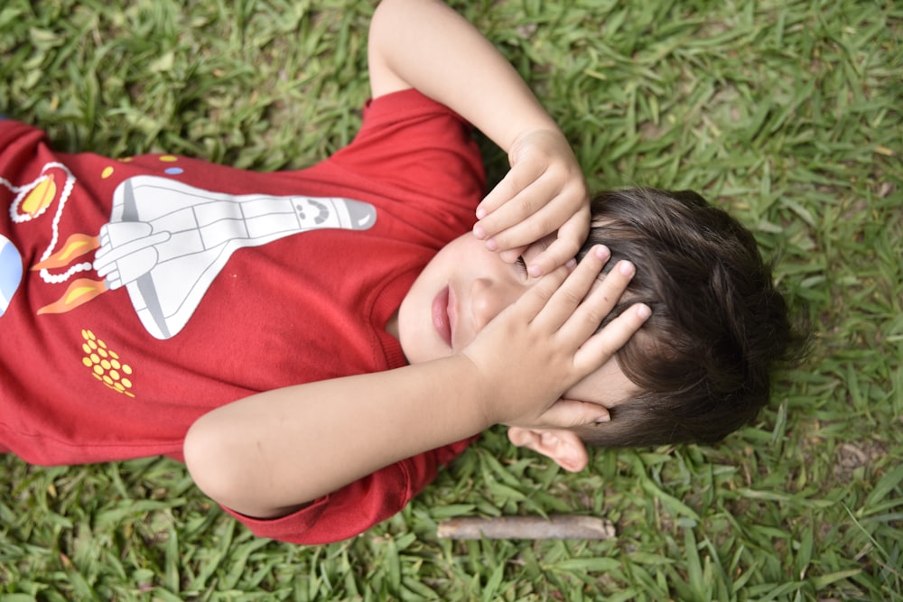 un ragazzino sdraiato sull'erba che si porta le mani al viso