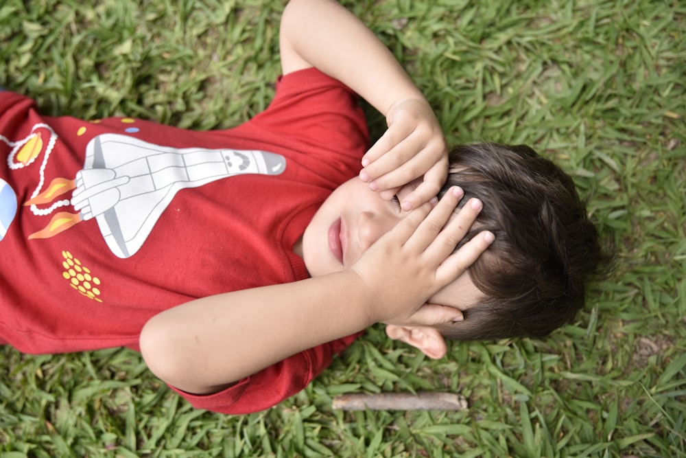 a young boy laying on the grass holding his hands to his face