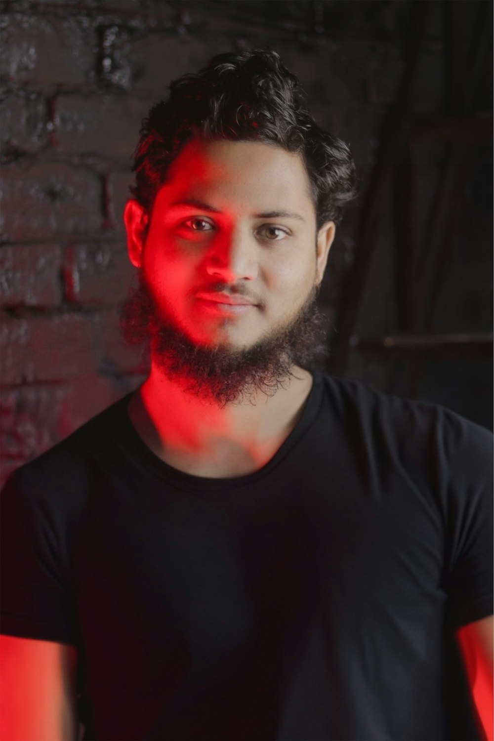 a man with a beard standing in front of a brick wall