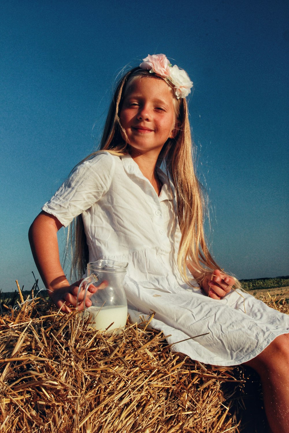 a little girl sitting on a pile of hay holding a glass of milk