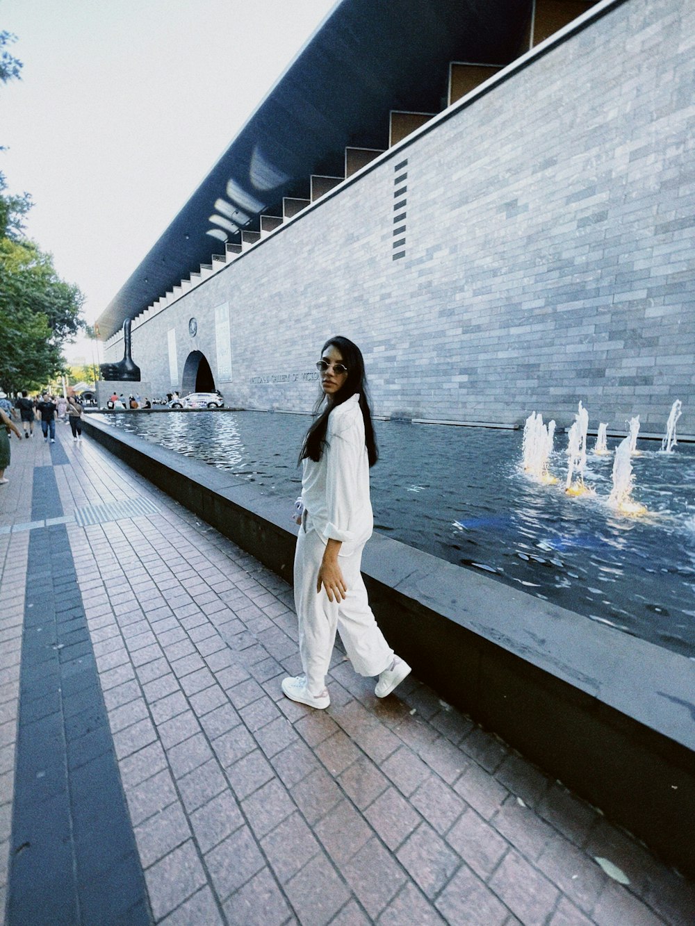 a woman walking down a sidewalk next to a fountain