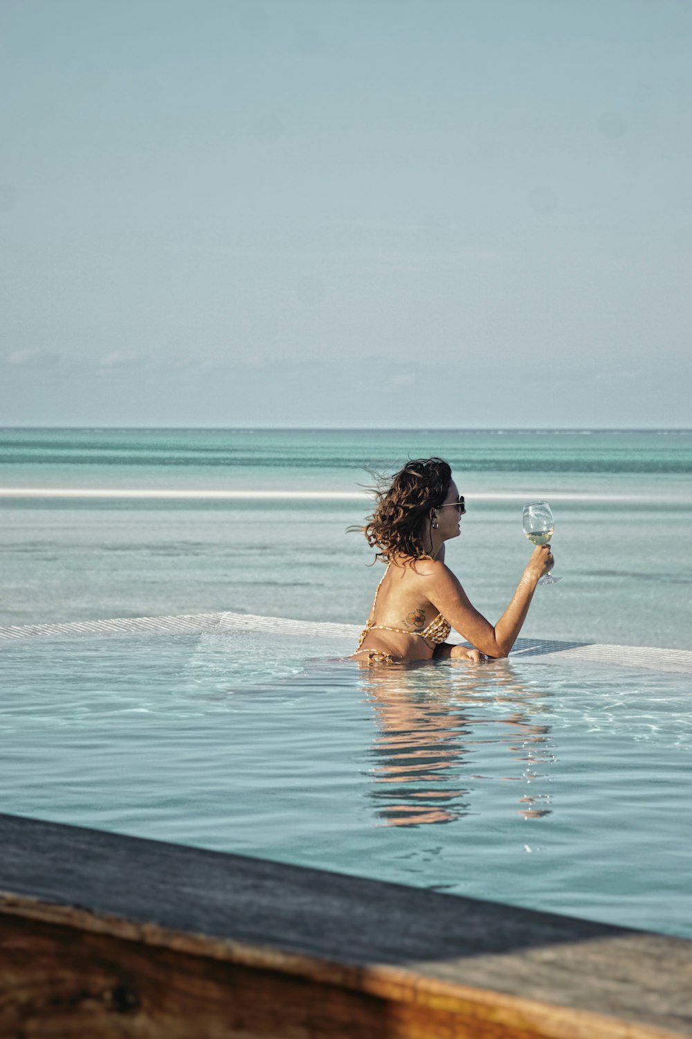 a woman sitting in a pool holding a glass of wine