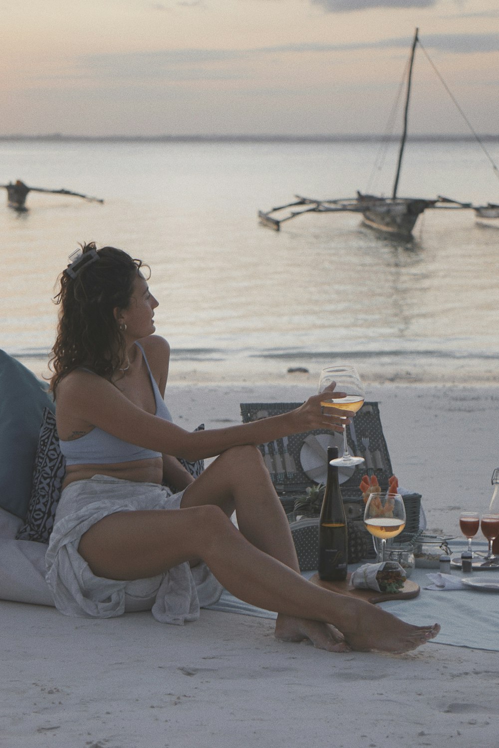 a woman sitting on the beach with a glass of wine