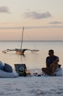 a man sitting on a beach next to a boat