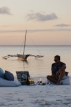 a man sitting on a beach next to a boat