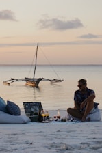 a man sitting on a beach next to a boat