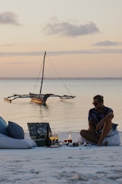 a man sitting on a beach next to a boat