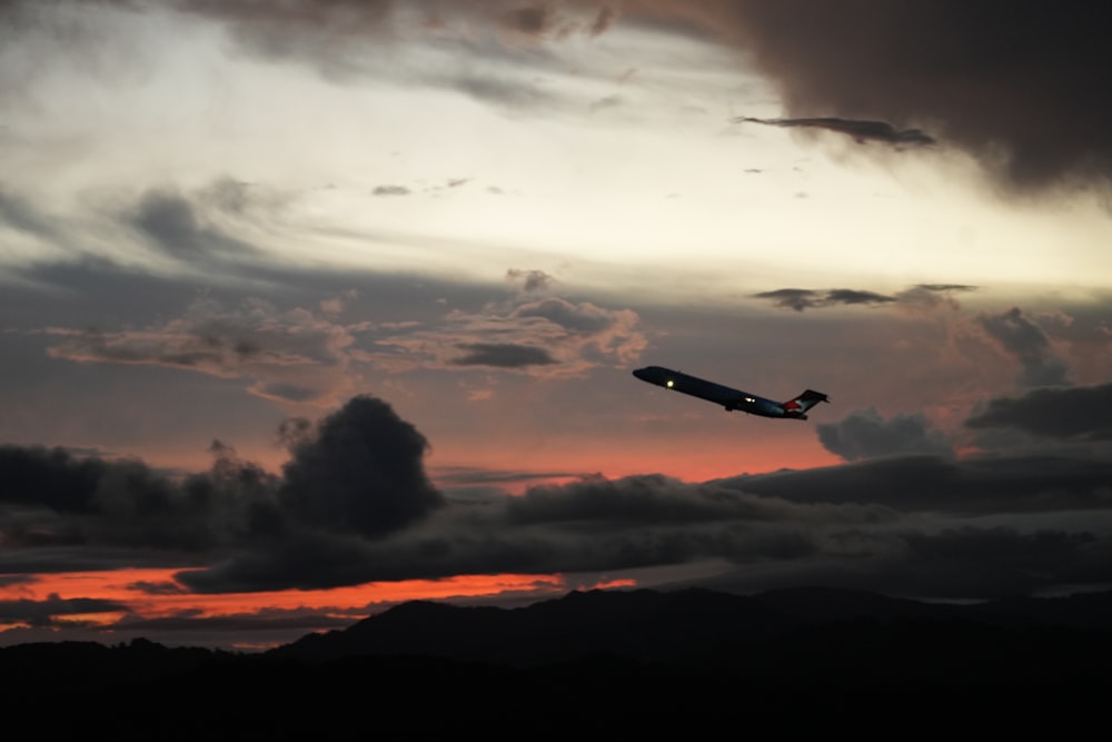 a plane flying through a cloudy sky at sunset