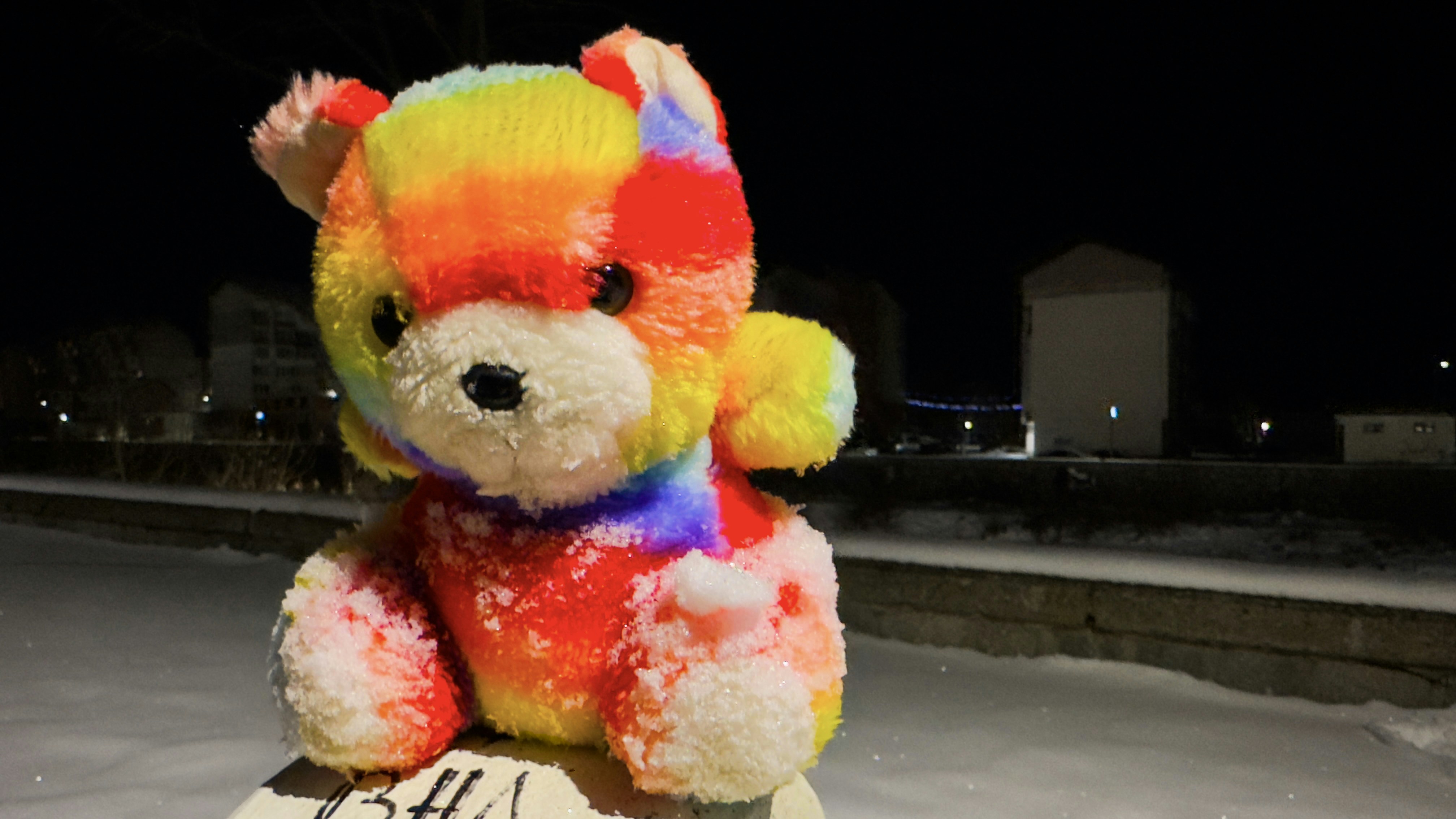 a teddy bear sitting on top of a sign in the snow