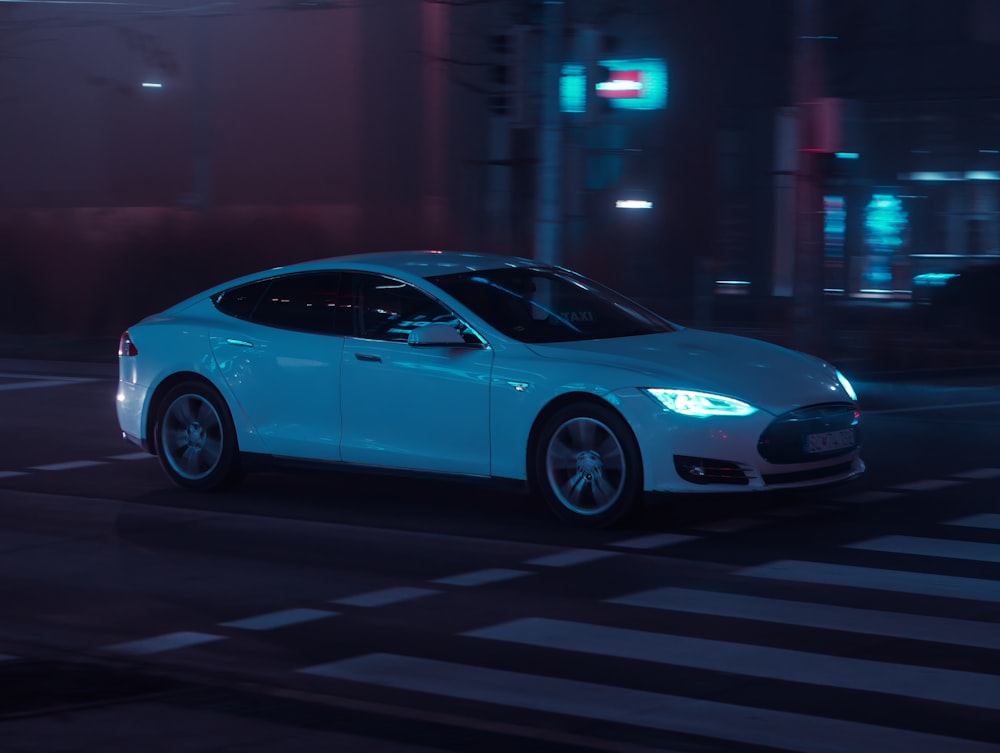 a white car driving down a street at night