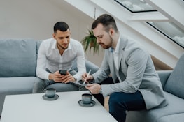 two men sitting on a couch looking at a cell phone