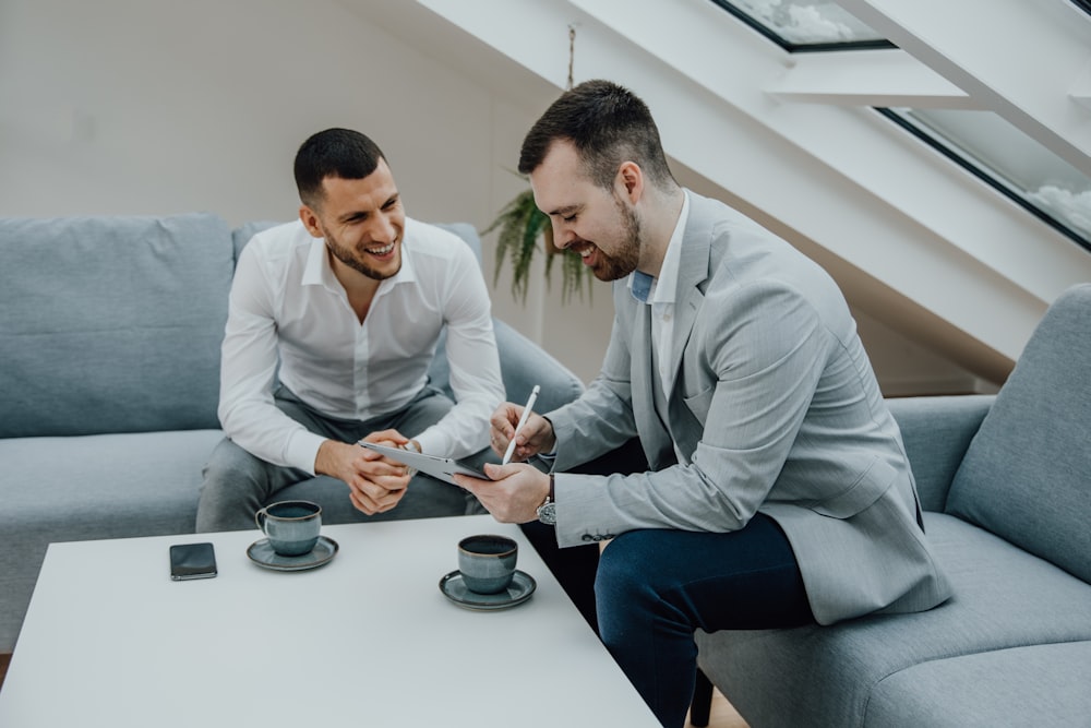 two men sitting on a couch signing something