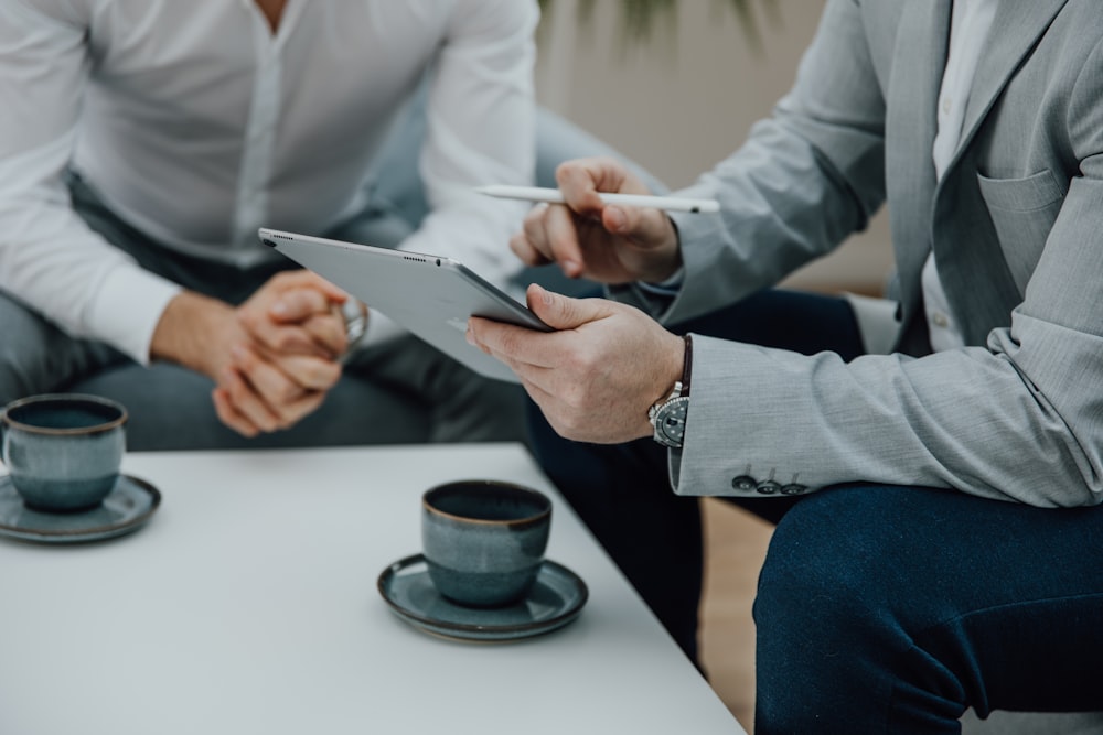 two men sitting at a table with a tablet