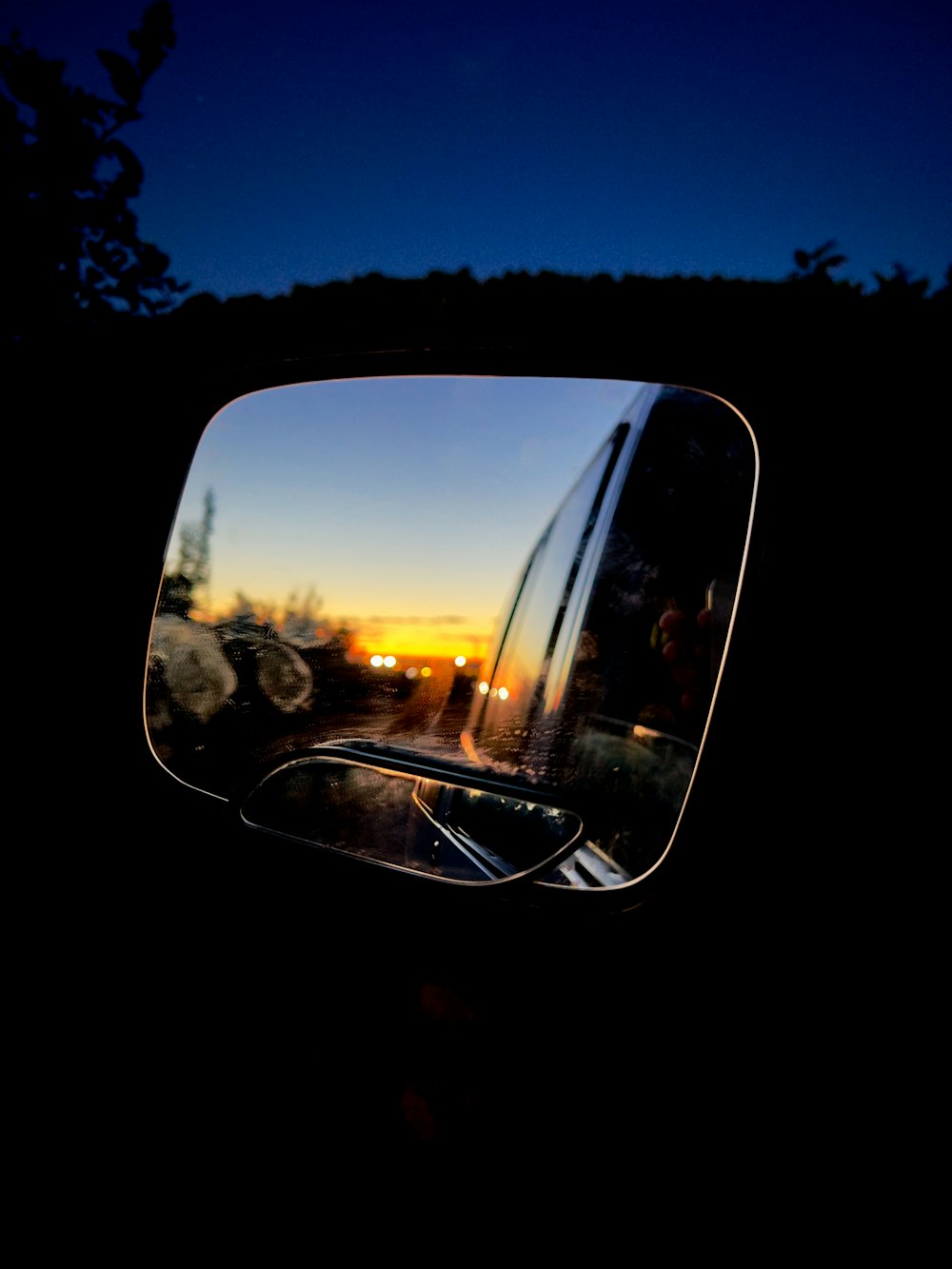 uno specchietto retrovisore che riflette un tramonto nello specchietto retrovisore laterale