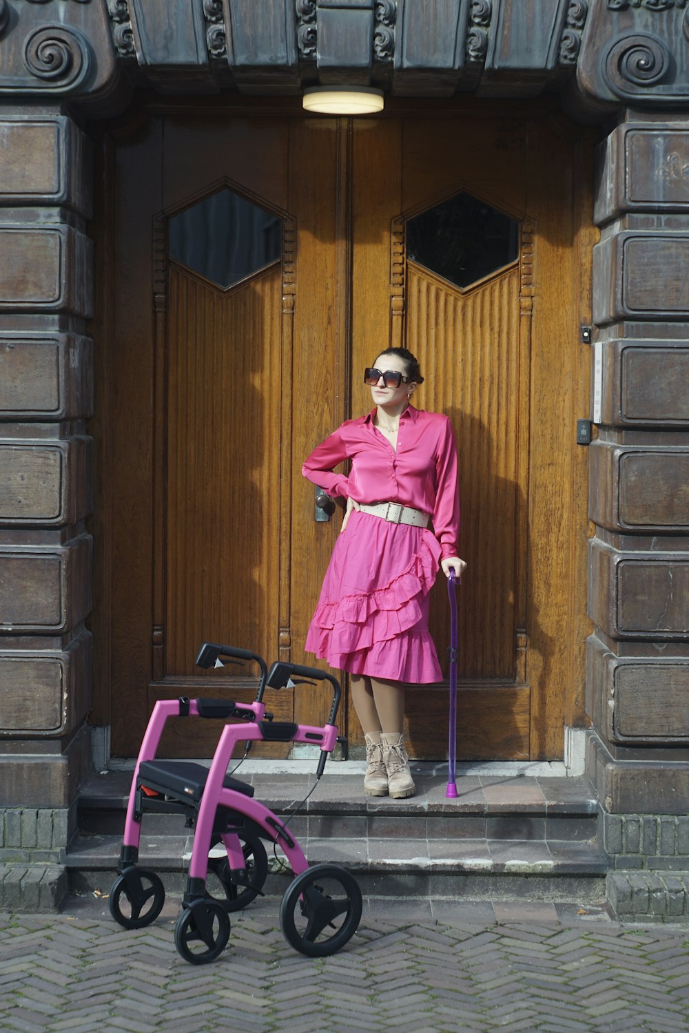 ピンクのワンピースを着た女性がベビーカーを持って立っている