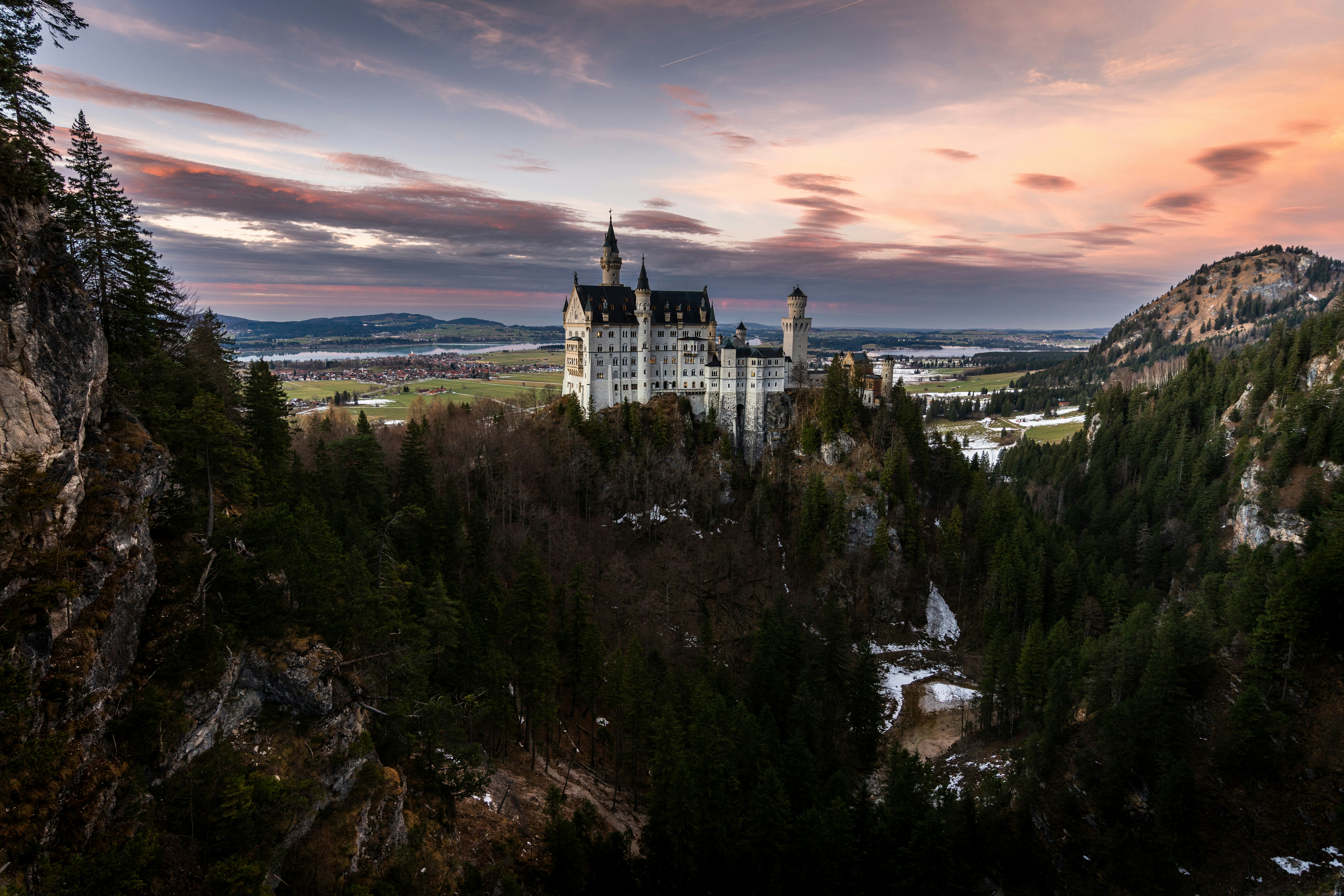 a castle on top of a mountain surrounded by trees, Neuschwanstein Castle, Germany, during sunset.