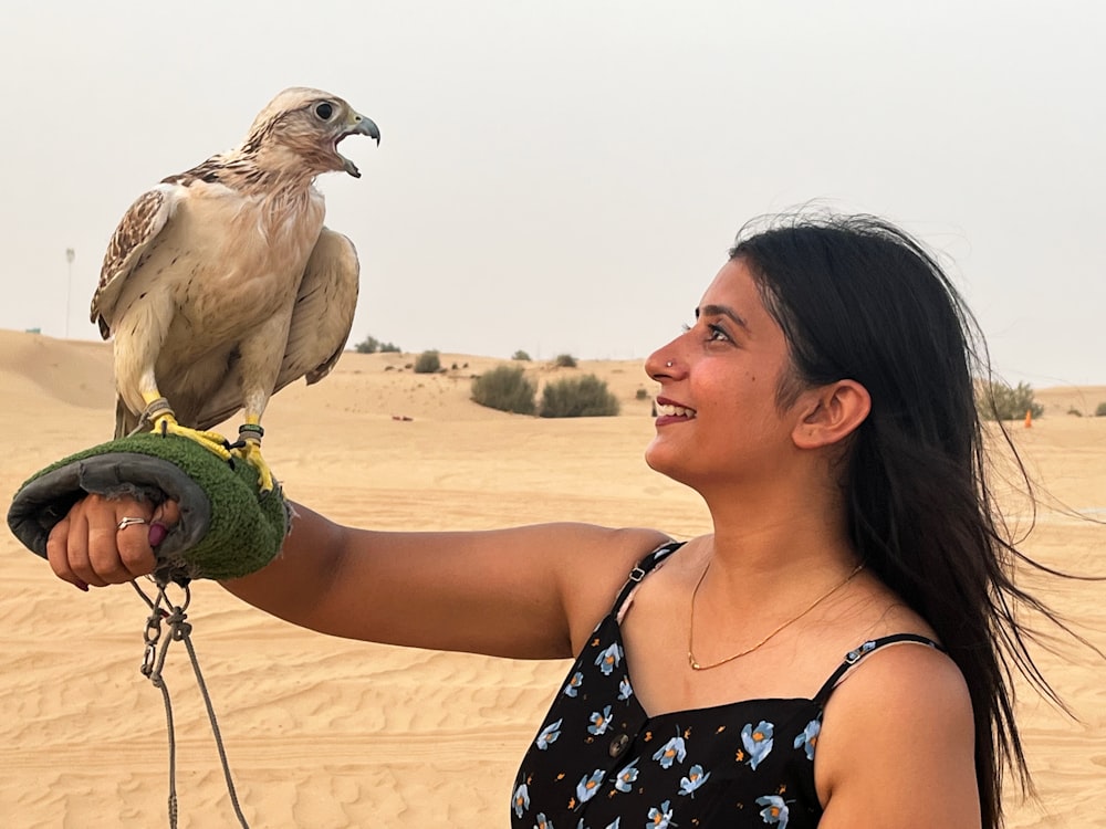 a woman holding a bird on her arm in the desert