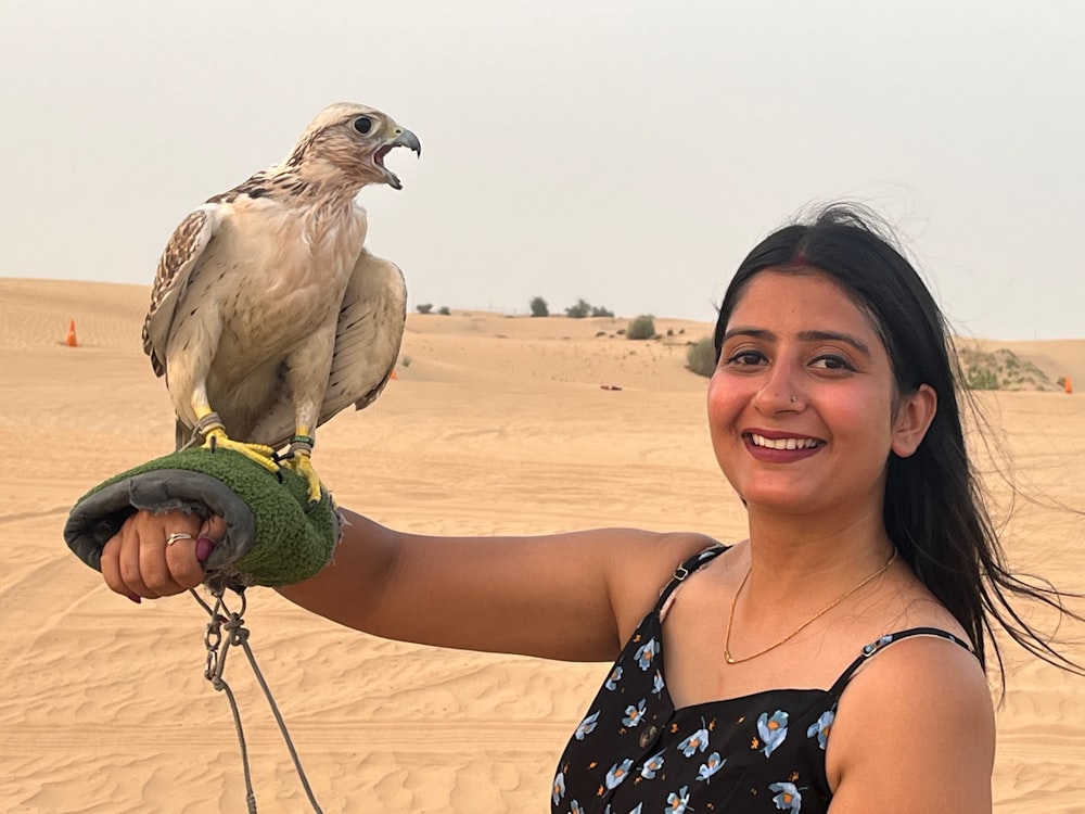 a woman holding a bird on her arm in the desert