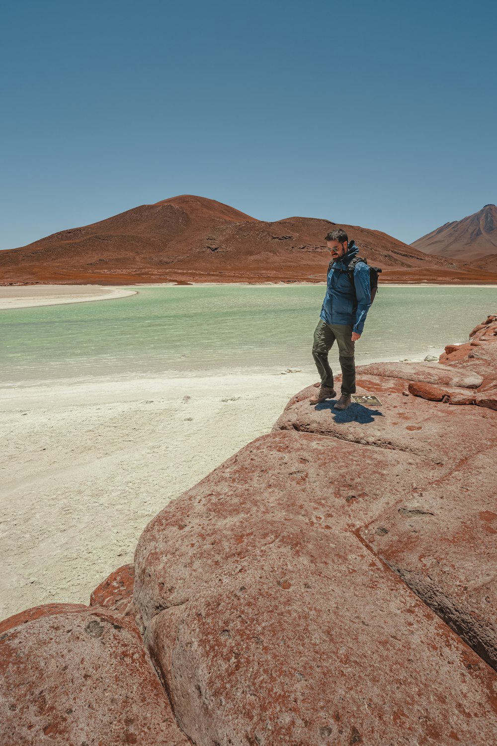 a man standing on top of a large rock next to a body of water