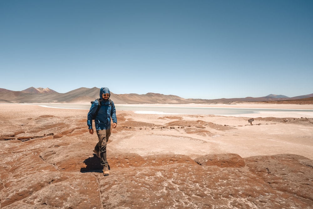a man in a blue jacket walking across a desert
