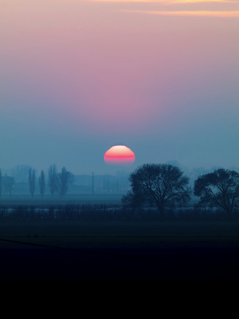 the sun is setting over a field with trees