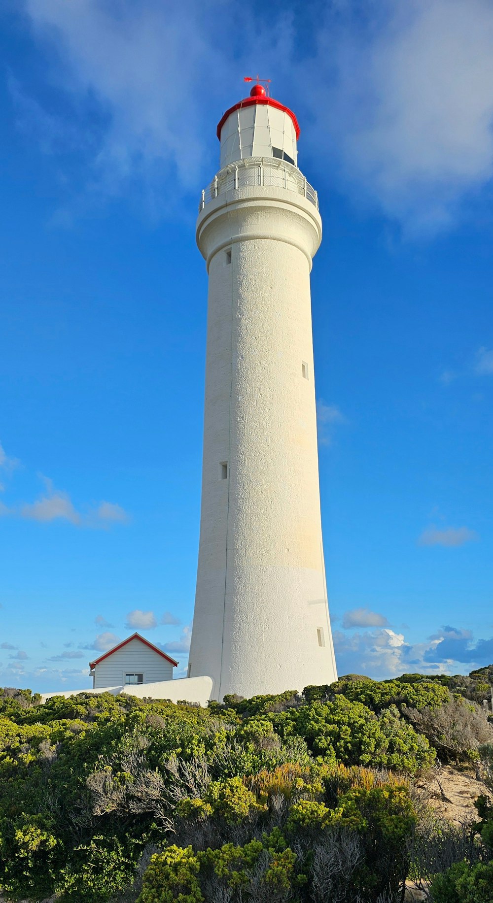 a white light house sitting on top of a lush green hillside